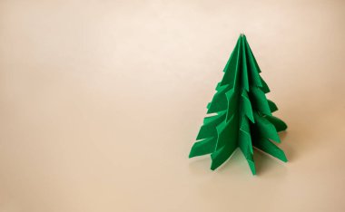 Mutlu Noeller ve mutlu yıllar bayrak konsepti, minimal stil. Açık bej arka planda duran ve fotokopi alanı olan yeşil renkli bir Noel ağacı..