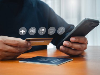 Seyahat ödeme planı, kredi kartının simgesi iş adamı elinde, akıllı cep telefonunu kullanarak uçuş ve otel rezervasyonları ve pasaportu için ahşap masada satın alıyor. Uluslararası gezi konsepti.