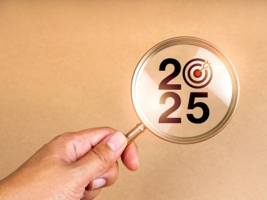 İş trendleri ve piyasa konseptiyle 2025 yılınız kutlu olsun. 2025 takvim numarası, insanların elinde büyüteç mercek hedef simgesi ile açık kahverengi zemin üzerinde fotokopi alanı, minimal biçim.