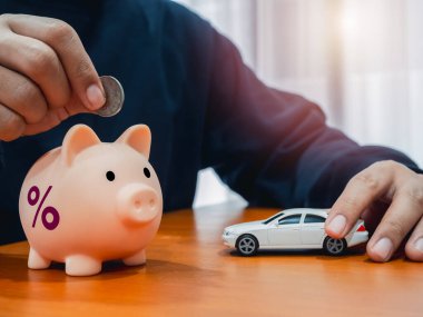 Araba vergisi, araç vergisi, geri ödeme, aylık borç ödemeleri, bütçe hesaplaması ve finansal sigorta kavramları. Para ve beyaz arabayı ahşap masaya koyarken domuz kumbarasının yüzde simgesi.