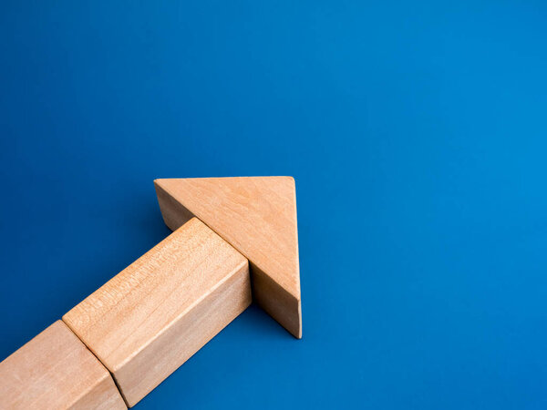 Moving forward, Business strategy growing up, growth process, leadership concept. Wooden cube blocks arranged as a large heading arrow, isolated on blue background with copy space, minimalist.