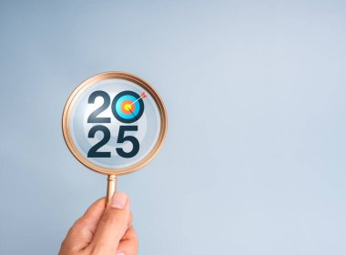 Piyasa eğilimleri, iş hedefi ve başarı konseptiyle mutlu yıllar 2025. 2025 takvim numarasına sahip hedef hedef hedef hedef simgesi insanların elinde büyüteç içinde açık gri zemin üzerinde fotokopi alanı ile.