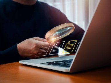 Elektronik belge kontrolü ve veri taraması online, dosya yöneticisi konsepti. Dizüstü bilgisayarla çalışırken, iş adamlarının elindeki büyüteçlerde sarı belge dosya simgesi görünür.