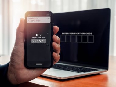 2FA ya da iki faktör doğrulaması, siber güvenlik kavramı. Şifre numarası anahtarı, elinde akıllı cep telefonu ekranında dizüstü bilgisayar tarafından giriş kodu için doğrulama kodu beklerken mesajlar gösteriliyor.