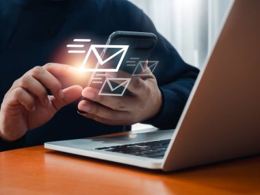 SMS gönderme, e-posta veya mesaj gönderme, iletişim teknolojisi kavramları. Zarfın hızlı taşınması, iş adamının telefonu kullanması ve dizüstü bilgisayarla çalışması sırasında dijital harf simgeleri görünmesi.