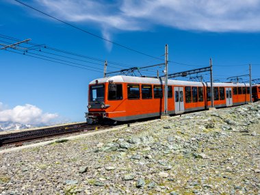 Matterhorn yakınlarındaki Gornergrat tren yolu üzerindeki kırmızı turist treni mavi gökyüzü arka planında güneşli bir günde, İsviçre Alpleri 'nde yaz mevsimi, İsviçre' nin Zermatt kentinde turizm beldesi.