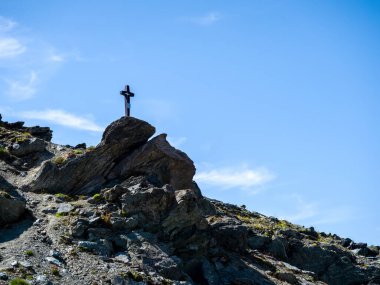 Mavi gökyüzü arkaplanındaki kayalık kayaların üzerinde fotokopi uzayı ile kara haç duruyor. İsviçre 'nin Zermatt kentindeki dağlarla turist yolu manzaralı uçurumda duran çapraz kesişen siluetler..