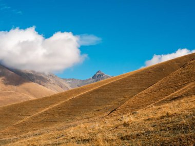 Sonbahar altın tepeleri, mavi gökyüzünde taş zirvesi güneşli bir günde bulut arkaplanı, Juta, Georgia 'da yürüyüş manzarası. Kahverengi ve sarı renkler küçük dağlarda temiz çimenler, güzellik manzarası.