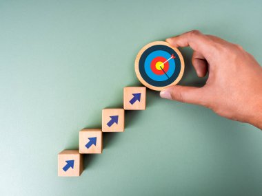 İş hedefi büyüme süreci, yeni hedef, yatırım planı, ekonomik iyileştirme kavramları. 3D hedef simgesini yeşil arka planda yükselen okla birlikte tahta küp blokların üzerine koy, minimalist.