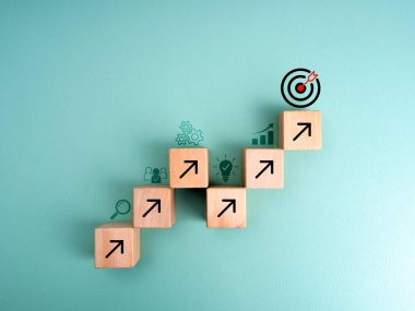 Liderlik kavramı için büyüme başarı sürecine sahip iş hedefi. Grafik adım olarak tahta küp bloklardaki ok işaretleri hedefin tepesine giderken mavi arkaplanda iş stratejisi simgeleri, asgari.