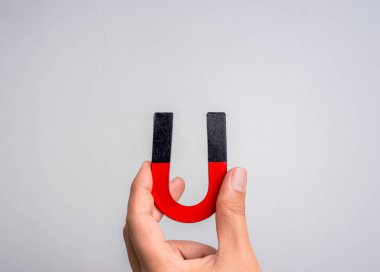 At nalı mıknatısı insan elinde. Mıknatıs tutan kişi, siyah ve kırmızı renkli, gri arka planda izole edilmiş, fotokopi alanı olan. Sosyal medya pazarlama araçları kavramsal, ticari nesne kavramı.