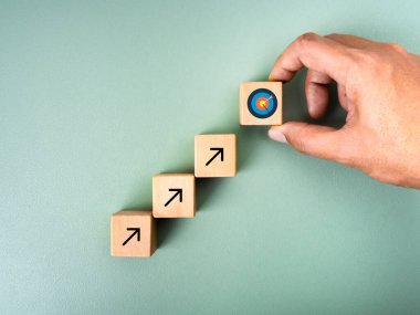 İş hedefi büyüme süreci, yeni hedef, yatırım planı, ekonomik iyileştirme kavramları. Elle hedef simgeyi, yeşil arkaplanda yükselen okla birlikte tahta küp blokların üzerine koy, en az stil.