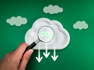 İklim değişikliği ve küresel ısınmayı sınırlamak için CO2 emisyonlarını azaltmak, net sıfır karbondioksit azaltma kavramı. Karbondioksit simgesi, beyaz buluta odaklı büyüteç, aşağı ok işaretleri, yeşil arkaplan.