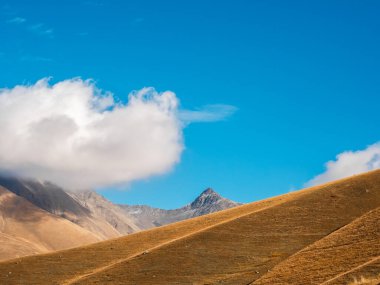 Sonbahar altın tepeleri, mavi gökyüzünde üçgen taş zirvesi güneşli bir günde bulut arkaplanı, Juta, Georgia 'da yürüyüş manzarası. Kahverengi ve sarı renkler küçük dağlarda temiz çimenler, güzellik manzarası.