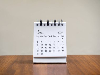 Organizatörün planlayıp hatırlatması için masa takviminin 2025 Mart sayfasındaki tahta masa zemininde duran beyaz arkaplan. Üçüncü aylı küçük masa takvimi, Mutlu yıllar 2025.