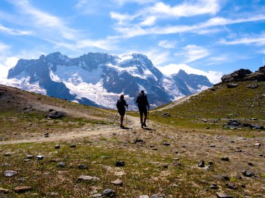 İki turist ya da gezgin çift İsviçre alp arkaplanındaki toprak yolda yürür, Zermatt, İsviçre 'deki yaz macerası.