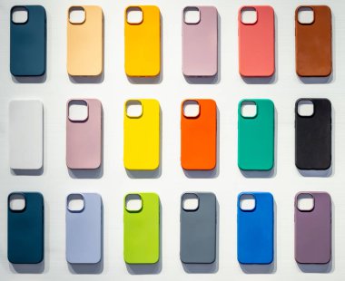 Beyaz arka planda izole edilmiş akıllı telefon için çok renkli kapaklar. Mobil aksesuar dükkanındaki beyaz duvarda, kamera lensleri için boş alanı olan renkli cep telefonu kılıfı..