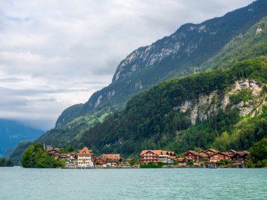Ev ve bina manzarası, yeşil tepe ve Brienz Gölü kıyısındaki köy, dağlar, doğal bulut ve sisli gökyüzü arka planı, seyahat manzarası..