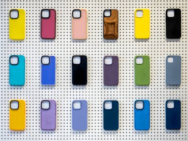 Beyaz tahta arka planda izole edilmiş akıllı telefon için arka kapaklar. Mobil aksesuar dükkanındaki beyaz duvarda, kamera lensleri için boş alanı olan renkli cep telefonu kılıfı..