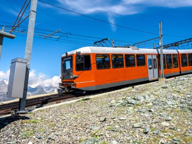 Matterhorn yakınlarındaki Gornergrat tren yolu üzerindeki kırmızı turist treni mavi gökyüzü arka planında güneşli bir günde, İsviçre Alpleri 'nde yaz mevsimi, İsviçre' nin Zermatt kentinde turizm beldesi.