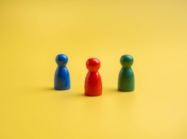 Kırmızı, yeşil ve mavi, sarı arkaplanda bir birlik sembolü olarak duran mandallı bebeklerin farklı renkleri. Liderlik, takım oluşturma, yetenek sahipleri, takım çalışması ve işbirliği kavramları.
