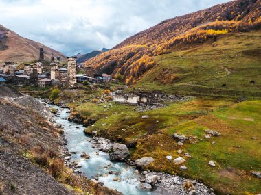 UNESCO 'nun mirası olan Ushguli köyünün önündeki nehir akıntısı manzarası, sonbahar dağları yakınlarında birçok ortaçağ kulesi evi, dikey stil, Gürcistan' ın Svaneti bölgesinde turistik cazibe.