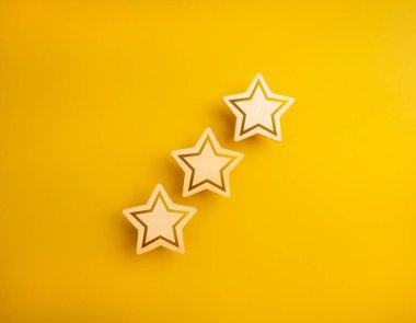 Üç parlayan ahşap yıldız reytingleri, sarı arka planda izole edilmiş, minimum stil. Yüksek kalite veya memnuniyet düzeyi, müşteri değerlendirmesi ve gözden geçirme, iş pazarlama kavramı.