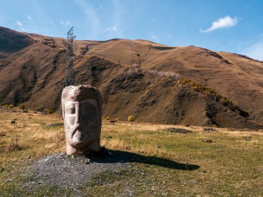 Sonbahar manzarası, devasa taş kafa, mavi gökyüzü arka planındaki dağların yakınındaki heykeller, Gürcistan 'daki turistik cazibe.