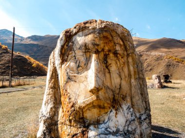 Sonbahar manzarası, devasa taş kafayla, mavi gökyüzünde dağlarda heykeller, Gürcistan 'da turistik cazibe..