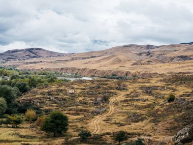 Uplistsikhe (Lord 's Fortress) yakınlarındaki sonbahar yeşili manzara, mağara şehrinin inanılmaz UNESCO dünya mirası alanı, bulutlu mavi gökyüzü arka planı, Georgia' daki ünlü seyahat cazibesi.