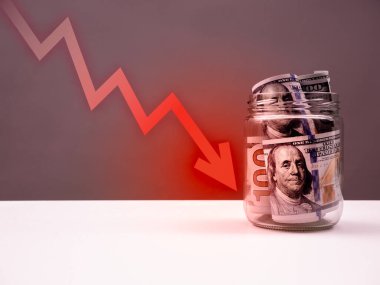 Kırmızı ok vuruşları Amerikan dolarına düşüyor. Para beyaz masa ve gri arka planda izole edilmiş cam kavanozun içinde duruyor. Borsa çöküşü, dolar zayıflaması, iş finans, para kavramı.
