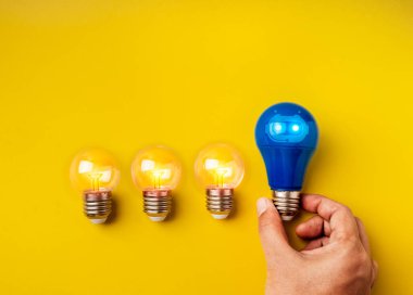 AI araçları teknoloji ve yenilik fikirleri, bireysellik, liderlik, yaratıcı kavramlar. Mavi ampulün üzerinde sohbet robotu simgesi, sarı arkaplanda küçük, berrak ampullerin yanında, minimalist.