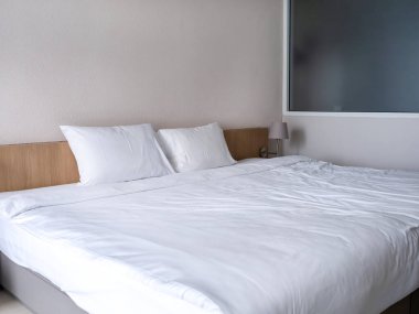 Misafir odasının içindeki beyaz temiz yatak odası, iki yastıklı beyaz battaniye basit ahşap yatak, buzlu cam bölme ve boş duvar, turist konaklama konsepti..