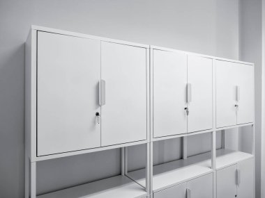 Üç beyaz çelik çalışma istasyonu ofis dolapları kilitleri ve rafları olan, mobilyalar sıraya dizilmiş, yeni işyerindeki beyaz temiz odaya yerleştirilmiş. İş, içişleri ve dekorasyon kavramı.