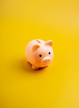 Üst manzara şirin pembe domuz kumbarası sarı renkli dikey arka planda, minimal tarzda izole edilmiş. Tasarruf parası, emeklilik bütçesi, özel masraf, kredi ve iş kredisi, bankacılık ve finans kavramı.