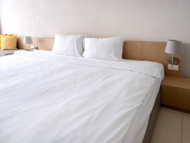 Misafir odasının içinde boş beyaz yatak odası manzarası, sade ahşap yatakta iki yastıklı beyaz battaniye, buzlu cam bölme ve boş duvar, turist konaklama konsepti..