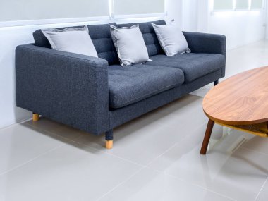 Boş gri kumaş kanepe koltuğu, oval ahşap masanın yanında yastıklar, temiz fayanslar, pencerenin yanında tekerlekli jaluziler, beyaz modern oturma odasında bekleme odası, kimse yok..