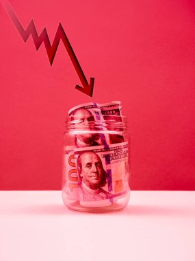 Dalgalanan ok atışları Amerikan dolarlarına düşer. Masadaki cam kavanozda nakit para biriktirir. Kırmızı tonlu arka plan. Borsa çöküşü, dolar zayıflaması, iş finansal çöküşü, para kavramı.