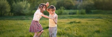 Yeşil bir alanda oynayan iki neşeli çocuk. Parlak renkler, doğal ışık. Aile, çocukluk ve açık hava temalı içerik için mükemmel. Geniş pankart kullanımı.