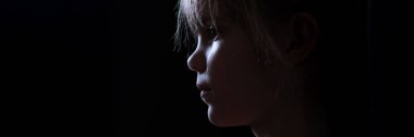 Düşük ışıktaki bir çocuğun yakın plan silueti. Dramatik, karamsar, havalı tonlu, duygusal ya da yansıtıcı temalar için uygun, geniş afiş biçimi.
