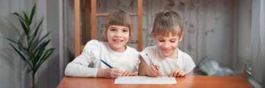 İki çocuk bir masada neşeyle resim çiziyor. Sıcak renkler ve yumuşak ışık davetkar bir atmosfer yaratır. Eğitim ve aile güdümlü tasarımlar için ideal. Kopyalama alanı olan geniş pankart.
