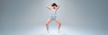 Gri arka planda neşeli pozlar veren canlı bir dansçı. Geniş pankart stili, reklam fitness veya moda için ideal kopya alanı sunuyor.