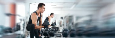 Spor salonunda dambılı kaldırmaya odaklanmış bir adam. Tarafsız tonlarda modern tarz. Fitness promosyonları ya da sağlık makaleleri için ideal. Kopyalama alanı olan geniş pankart.