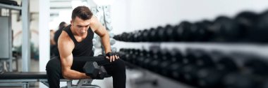 Modern bir spor salonunda dambılı kaldırmaya odaklanmış bir adam. Parlak ışık ve nötr tonlar güç ve adanmışlığı işaret ediyor. Fitness terfileri ve sağlık blogları için ideal.
