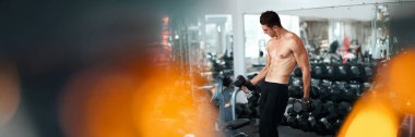 Spor salonunda dambılları kaldıran kaslı bir adam. Modern tarz, sıcak tonlarda, kopyalama alanı olan. Fitness promosyonları ve spor salonu reklamları için ideal..