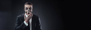 İskelet makyajlı bir adam karanlık ve dramatik bir tarzda şaşırmış görünüyor. Cadılar Bayramı, korku teması ya da pazarlama için mükemmel. Kopyalama alanı olan geniş pankart.