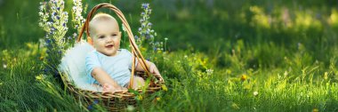 Gülümseyen bir bebek yeşillik ve çiçeklerle çevrili bir sepetin içinde oturur. Parlak ve neşeli tasarım bebeklerle ilgili terfiler için mükemmel. Kopyalama alanı olan geniş pankart.