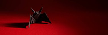 Siyah origami yarasası koyu kırmızı arka planda. Karanlık tonlu minimalist stil, Cadılar Bayramı teması ve tasarım kullanımı için uygun. Kopyalama alanı olan geniş pankart.