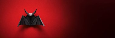 Kırmızı arkaplanda siyah bir origami yarasası. Karanlık gölgeli minimalist tarz, Cadılar Bayramı teması için uygun. Kopya alanı ile geniş afiş içerir.