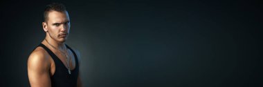 Siyah kolsuz tişörtlü ciddi bir adamın portresi. Siyah arka planda, geniş afiş ve fotokopi alanı var. Fitness, reklam ve editoryal kullanım için ideal.
